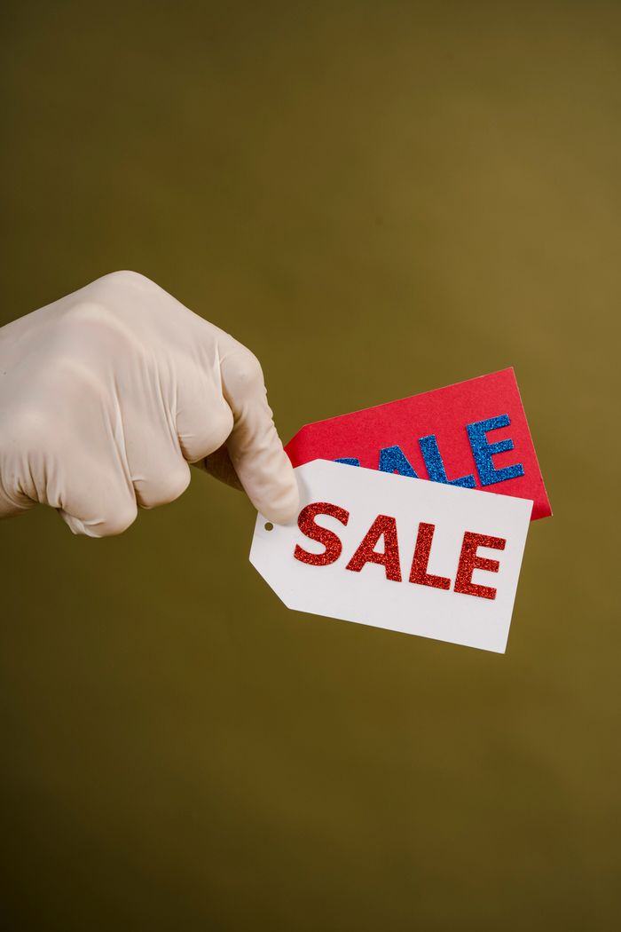 Gloved hand holding red and white sale tags on a green background, emphasizing shopping and discounts.