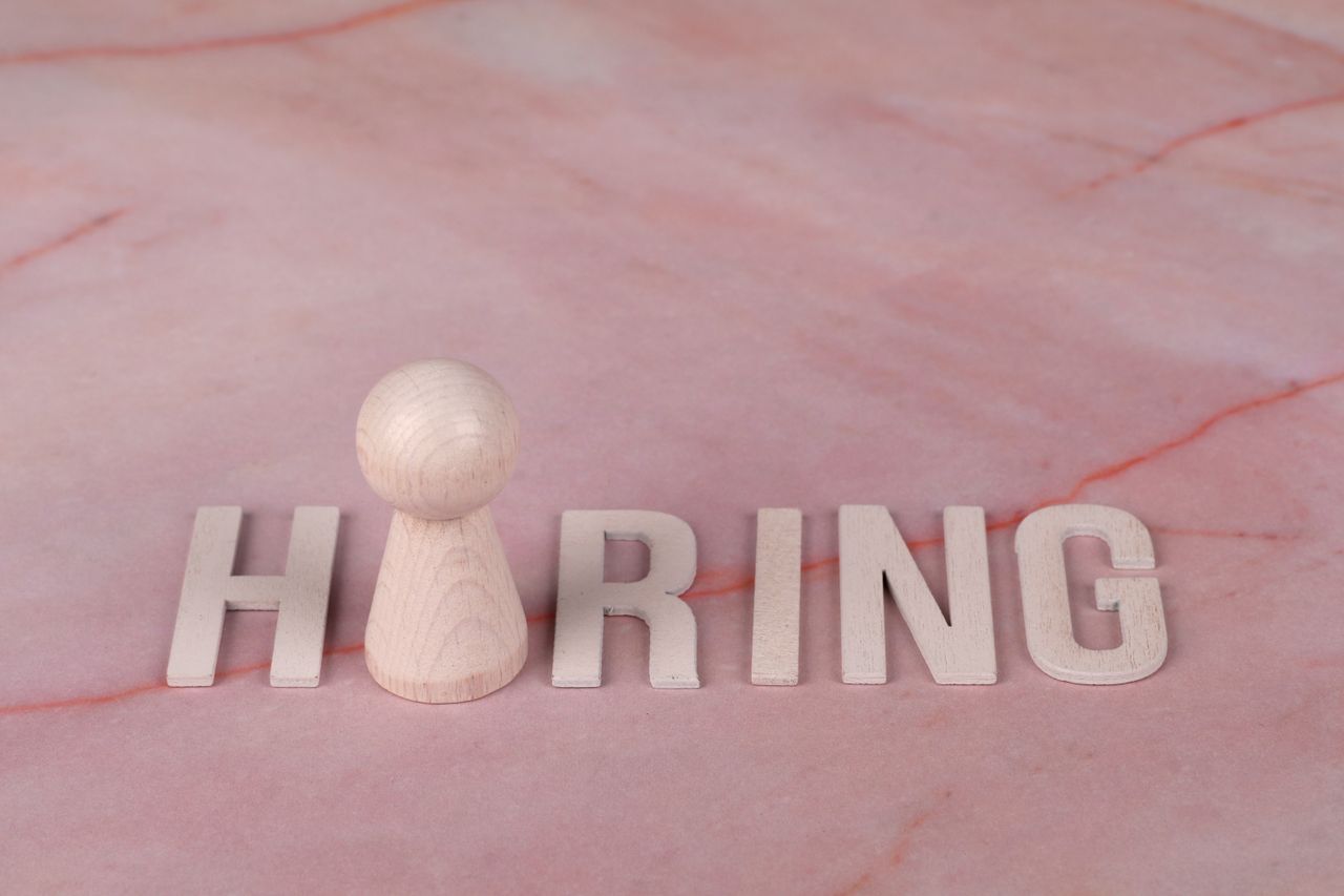 Wooden letters spelling hiring on pink marble background with a peg.